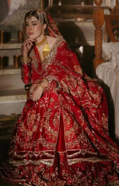 a woman in a red and gold wedding dress sitting on a chair with her hand under her chin