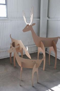 three cardboard deer standing next to each other in front of a white wall and window