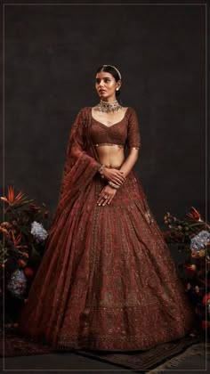 a woman in a red and gold lehenga is standing with her hands on her hips