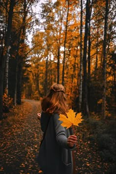 a woman walking down a path holding a leaf in her hand and looking up at the sky