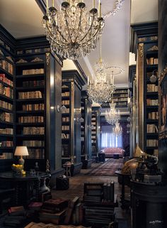 a library with chandelier, bookshelves and couches