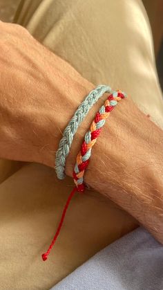 a person wearing two different colored bracelets on their arm with red string attached to it