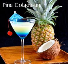 a pineapple next to a blue drink in a glass on a wooden serving tray