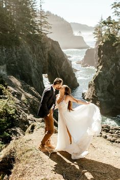 a bride and groom kissing on the cliff overlooking the ocean