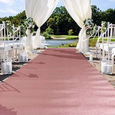 an outdoor wedding ceremony with white drapes and pink carpeted aisle leading into the water