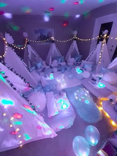 a room filled with lots of white beds covered in blankets and pillows next to christmas lights