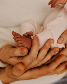 two hands holding a baby's head in the middle of their body, while another hand holds it up