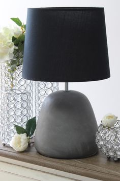 a table lamp sitting on top of a dresser next to a vase filled with flowers