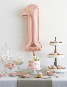 a pink number one balloon sitting on top of a table filled with cakes and desserts