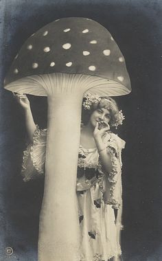 a woman standing next to a mushroom with her hand on her face and holding it up in the air