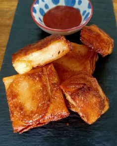 some fried food on a black plate next to a bowl with dipping sauce in it