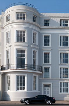 a black car parked in front of a large white building with balconies on the top floor