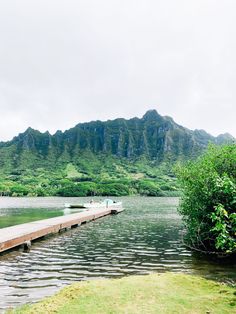 two boats are docked at the end of a dock in front of mountains and water