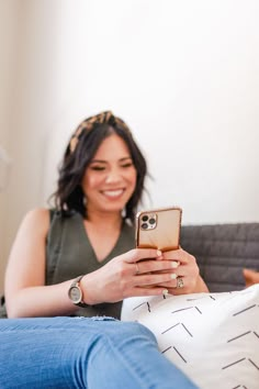 a woman sitting on a couch looking at her cell phone while holding it in her hand