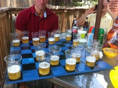 a man standing in front of a blue checkerboard table filled with glasses and beer