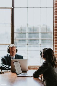 two people sitting at a table with laptops and headphones in front of them