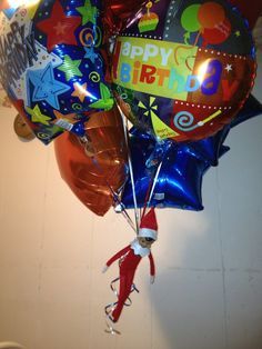 a bunch of balloons that say happy birthday and have an elf on them hanging from the ceiling