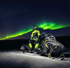 a man riding on the back of a snowmobile in front of an aurora bore