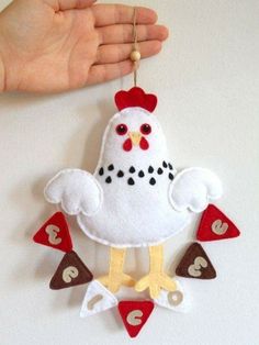 a hand holding a white and red chicken ornament on a string with hearts