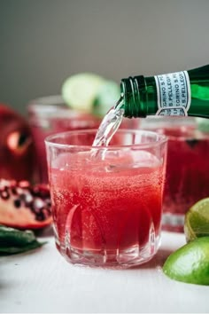 a bottle of water being poured into a glass filled with red liquid and limes