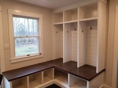 an empty room with white walls and wooden bench in front of the window, along with several open shelving units