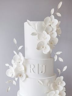 a three tiered white wedding cake with flowers on the top and initials on the side