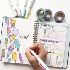 a person holding a pen and writing on an open planner book next to washi tape