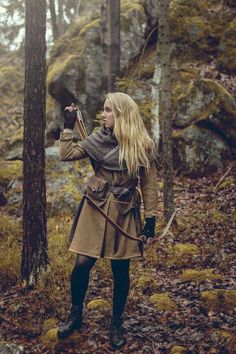 a woman standing in the woods holding an arrow