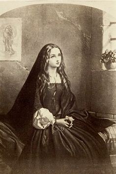 an old black and white photo of a woman in a long dress sitting on a bed