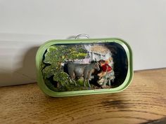 a small tin case sitting on top of a wooden table next to a cow and dog