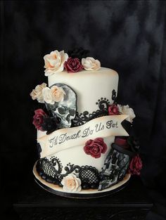 a three tiered cake decorated with skulls, roses and ribbon that says dead or just