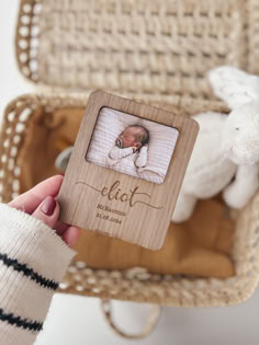 a person holding up a small wooden frame with a baby's photo on it