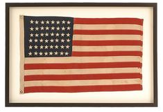 an old american flag is displayed in a black frame on a white wall with a brown border