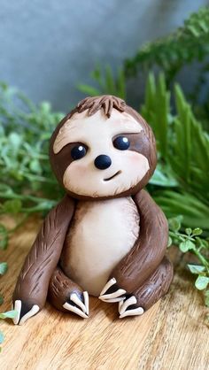 a small toy sloth sitting on top of a wooden table next to green plants