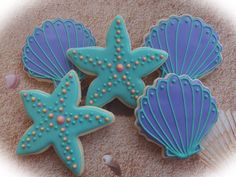 three decorated cookies in the shape of starfishs and seashells on sand