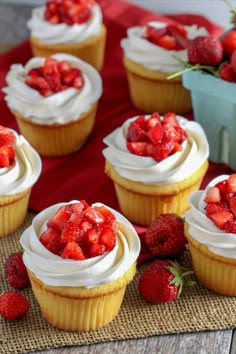 several cupcakes with white frosting and strawberries on the top are sitting on a mat