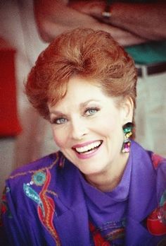 a woman with red hair and blue eyes smiles at the camera while sitting in a chair