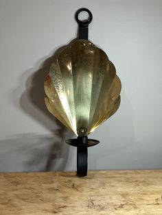 a brass shell lamp sitting on top of a wooden table next to a white wall