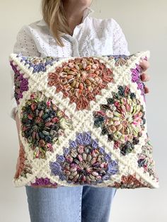 a woman holding a crocheted pillow with flowers on it