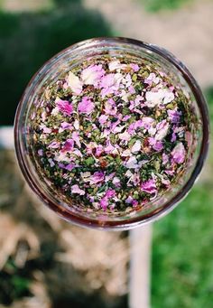 a glass filled with pink flowers sitting on top of a grass covered field next to a metal pole