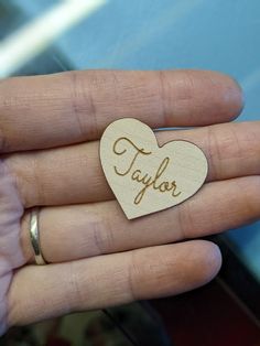 a person holding a small wooden heart with the word taylor written in cursive writing on it