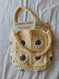 a crocheted purse sitting on top of a white bed next to a book