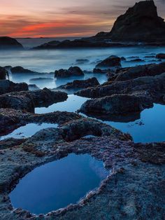 the sun is setting over an ocean with rocks and small puddles in the water