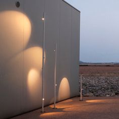 three lights are on the side of a building near some rocks and grass at dusk