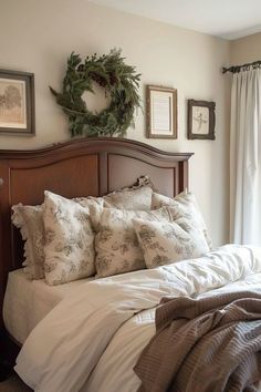 a bed with pillows and blankets on top of it in front of a window next to a wreath