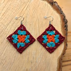 a pair of crocheted earrings sitting on top of a piece of wood