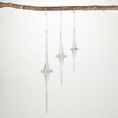 three clear glass ornaments hanging from a tree branch in front of a white wall and floor