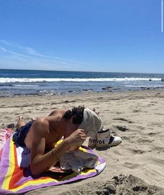 a man laying on top of a beach next to the ocean while holding a cell phone