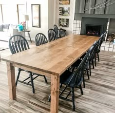 a large wooden table surrounded by black chairs in a room with wood floors and a fireplace