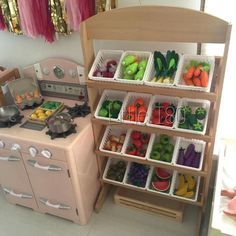 a toy kitchen with lots of fruits and veggies in bins on the shelves